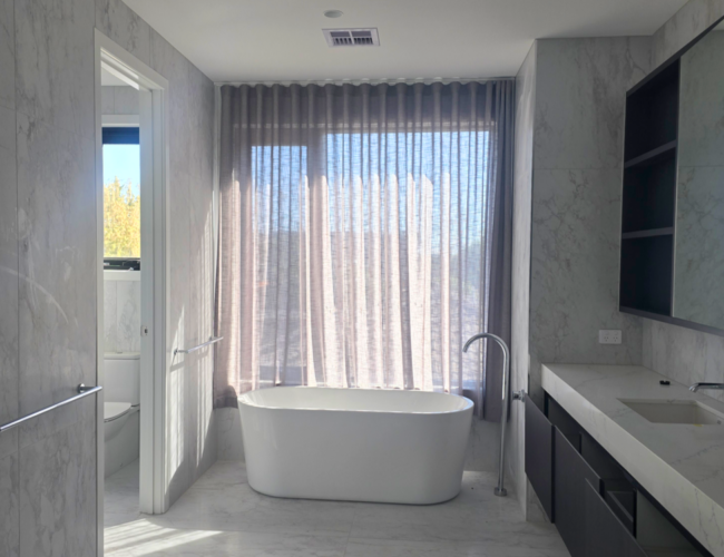 Spa-like bathroom with wavefold sheer tucked behind bathtub
